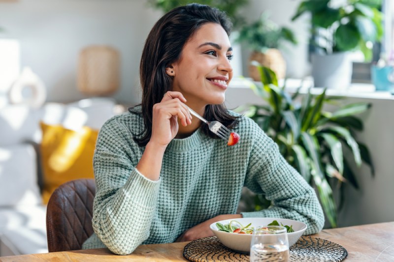 Woman smiling as she eats a salad with strawberries and no dressing.